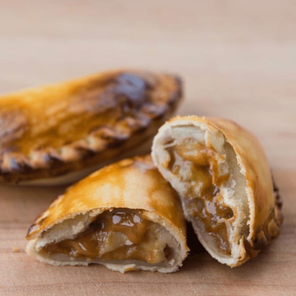Two golden-brown JAVI’S COOKING Argentinian empanadas, one sliced open revealing a dulce de leche filling.