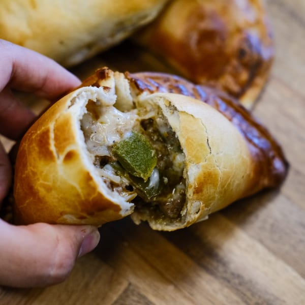 Hand holding a JAVI’S COOKING Argentinian empanada, split open to show a savory filling.