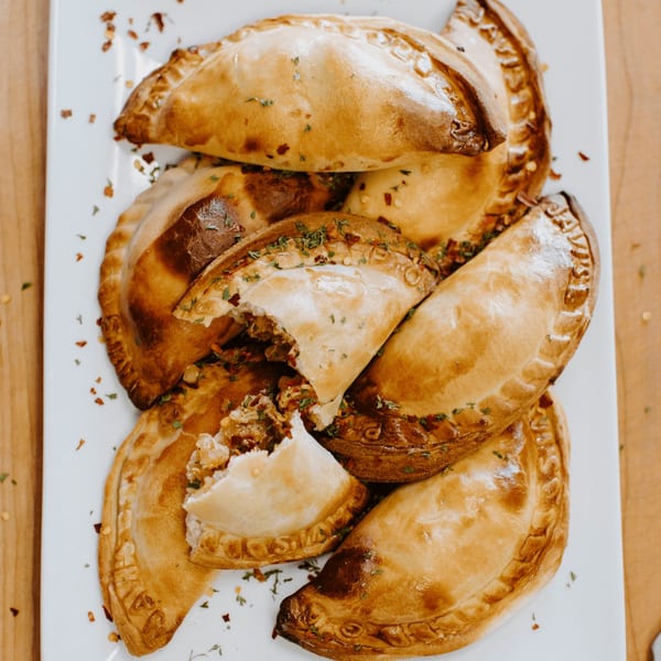 A platter of golden-brown JAVI’S COOKING Empanadas Argentinas, some broken open to show the savory filling.