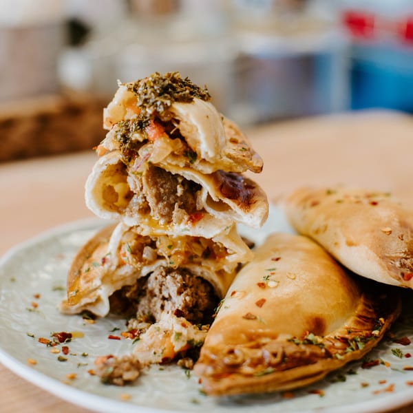 A stack of JAVI’S COOKING Argentinian empanadas, some cut open to show the savory filling.