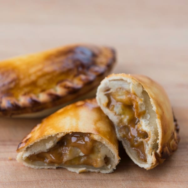 Two golden-brown JAVI’S COOKING Empanadas Argentinas, one cut open revealing a sweet, gooey filling.