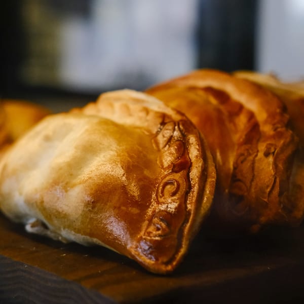 Close-up of golden-brown Argentinian empanadas with crimped edges, arranged on a dark surface.