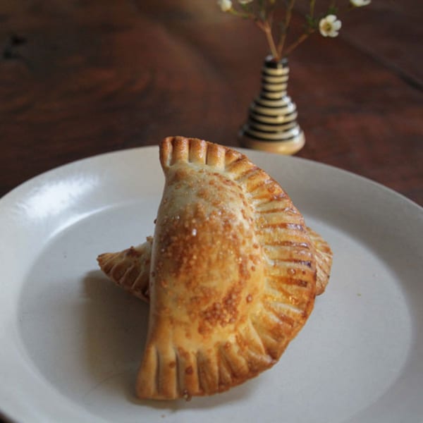 Two golden-brown JAVI'S COOKING Empanadas Argentinas on a white plate with a small vase in the background.
