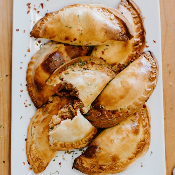 A platter of JAVI’S COOKING Argentinian empanadas, some broken open to show the savory filling.