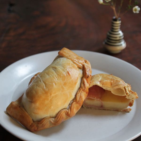Two golden-brown JAVI’S COOKING empanadas on a white plate, one sliced open revealing a creamy filling.