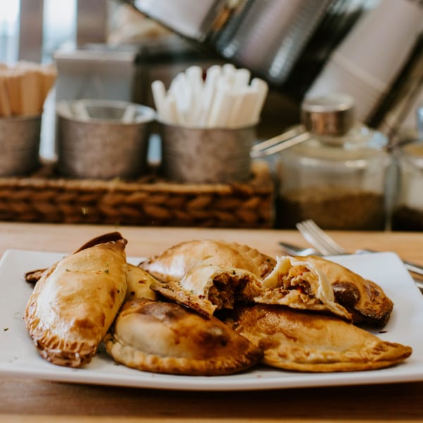 A plate of golden-brown JAVI’S COOKING Empanadas Argentinas, one broken open to show the filling.